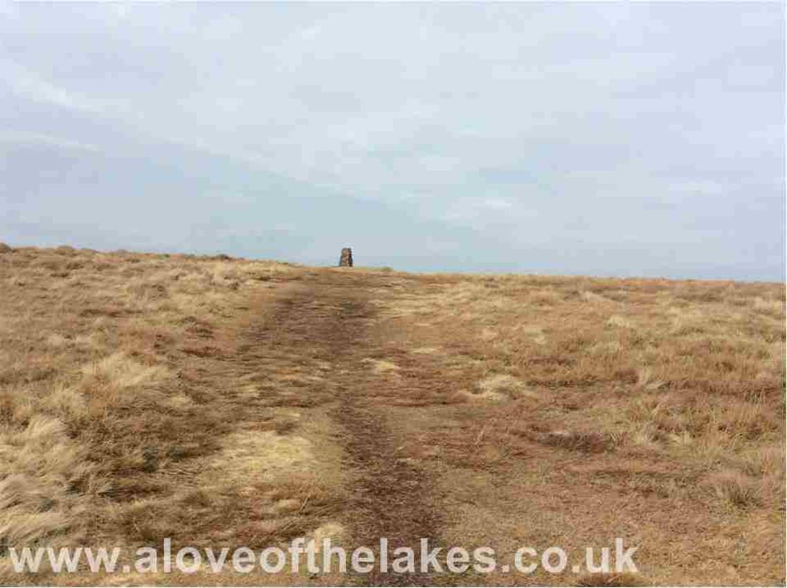 After a short distance, the crest of the slope is reached and the ground levels up to reveal the summit trig point cairn

